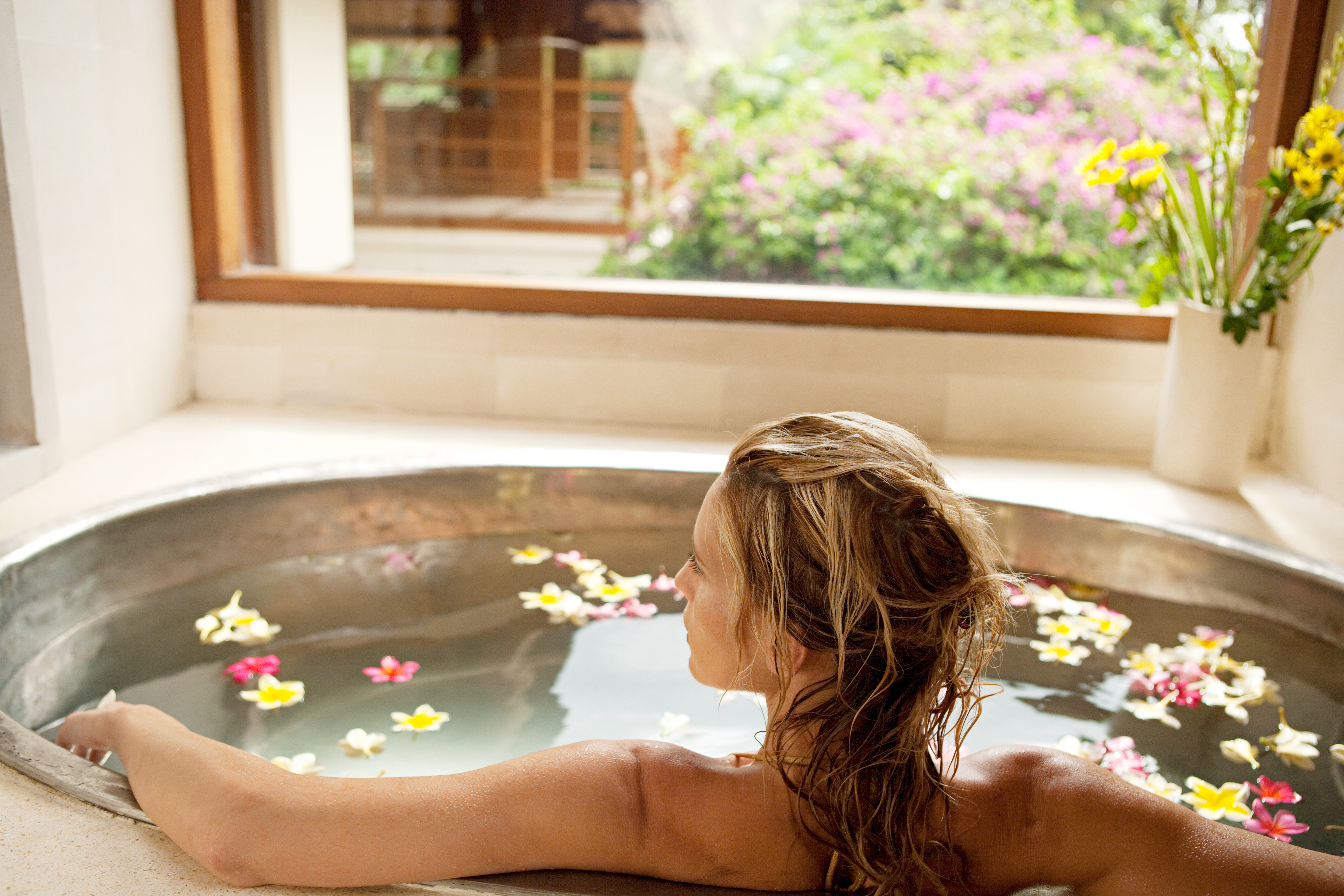 Back view of a young woman bathing in a health spa's flower bath.